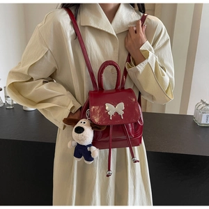 Détail d'un mini sac à dos en cuir verni rouge foncé avec boucle papillon et peluche