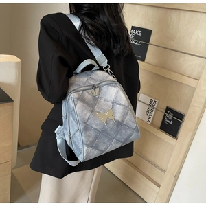 Woman wearing quilted light blue denim backpack with golden butterfly detail on back