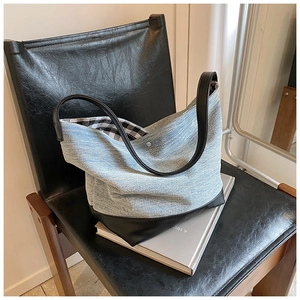 Detail of blue denim tote bag with black leather base and checkered lining on a chair