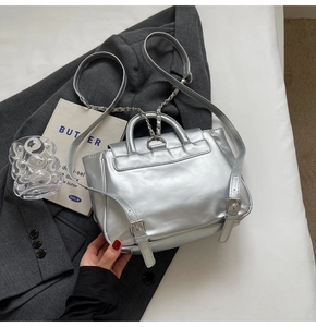 Détail d'un sac à dos argenté métallisé avec bretelles à chaîne sur un fond de costume