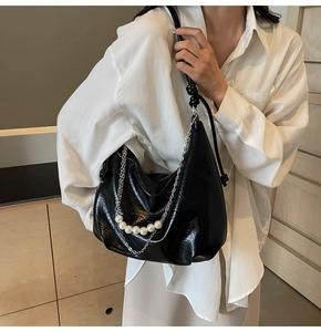 Dettaglio della borsa hobo nera a pieghe con catena d'argento e perle indossata