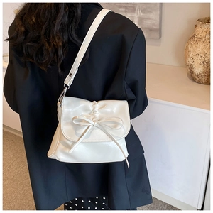 Detail of cream pleated crossbody bucket bag with bow accent on a black blazer jacket