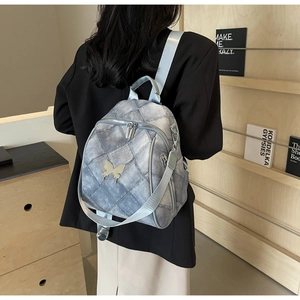 Detail of light gray quilted mini backpack featuring a metal butterfly and dual straps