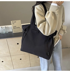 Detail of black canvas tote bag showing side drawstring and brand woven label