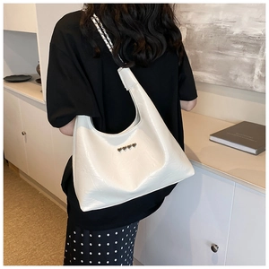Close-up of white hobo bag with silver heart studs and chain strap worn by a model