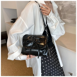 Detail of glossy black pleated bucket bag with bow accent worn by a model