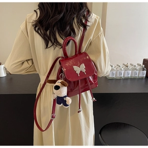 Détail du sac à dos rouge brillant avec boucle papillon argentée et charm chien en peluche