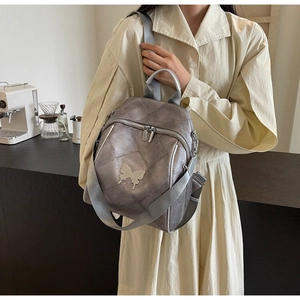 Macro detail of grey quilted backpack with metallic butterfly pendant and top handle