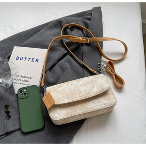 Beige canvas crossbody bag with orange leather strap on a grey suit jacket