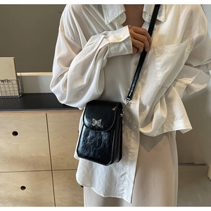 Close-up of black glossy crossbody phone bag featuring a silver metal butterfly clasp