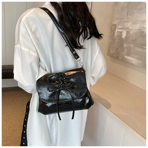 Detail of glossy black PU leather crossbody bag featuring a delicate bow tie decoration