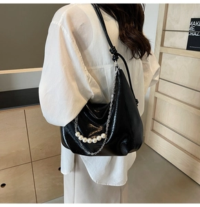 Dettaglio borsa hobo in pelle verniciata nera con catena d'argento e perle bianche