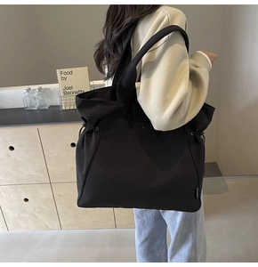 Detail of adjustable side drawstring and woven label on black canvas tote bag