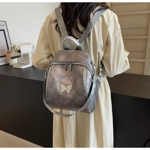 Detail of silver metallic quilted backpack featuring a 3D metal butterfly decoration