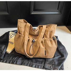 Detail of khaki nylon tote bag with drawstring side pockets on black leather jacket