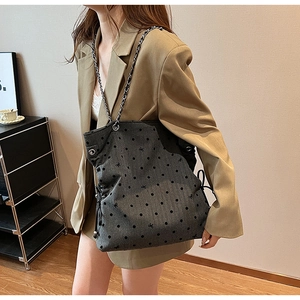 Detail of grey polka dot tote bag featuring chain strap and side drawstring closure