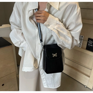 Detail of black glossy crossbody phone bag with silver butterfly metal ornament