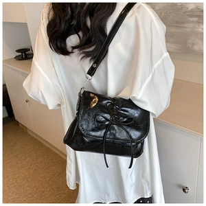 Detail view of a black pleated leather bucket bag with bow on a model's shoulder