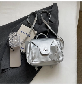 Détail d'un mini sac à dos argenté métallisé avec pendentif cœur sur blazer gris
