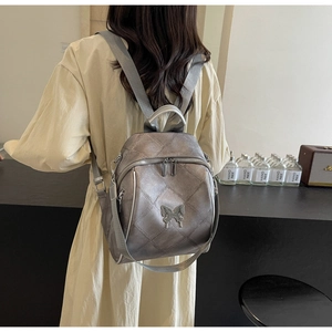 Detailed view of silver-grey quilted backpack with metallic butterfly charm and straps
