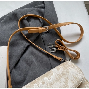 Detail of adjustable leather strap and metal hooks on textured designer crossbody bag