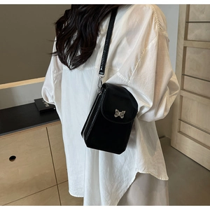 Detail of a black leather crossbody phone bag with a silver butterfly buckle on a model