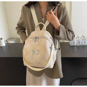 Detail of cream quilted backpack with silver butterfly charm and metal zip closure