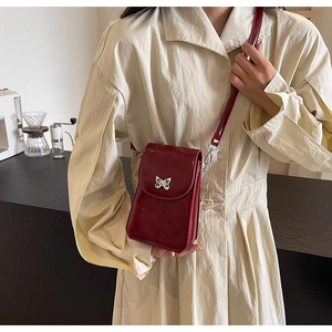 Detail of burgundy patent leather phone bag with silver butterfly buckle on beige dress