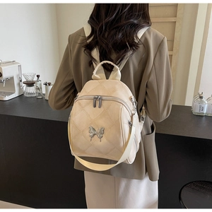 Rear view of beige quilted leather backpack with metal butterfly on female model