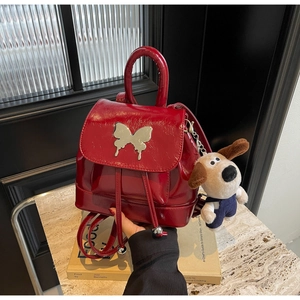 Détail d'un sac à dos rouge verni avec boucle papillon argentée et pendentif de chien
