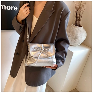 Silver pleated shoulder bag with bow detail styled with a brown blazer and minimalist decor
