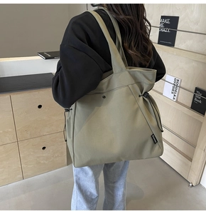 Detail of canvas tote bag showing side drawstring buckle and large capacity on model back