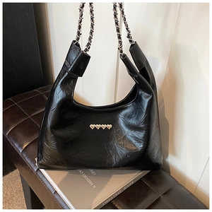 Close-up of black wrinkled leather tote bag with silver heart charms and chain strap