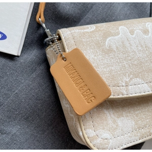 Detail shot of a beige shoulder bag featuring a leather brand tag with MIKA XQI & BAG logo