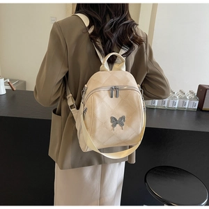 Detail of light beige quilted backpack featuring a silver butterfly charm and adjustable straps