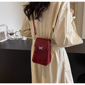 Detail of red glossy crossbody phone bag with silver butterfly clasp and slim shoulder strap