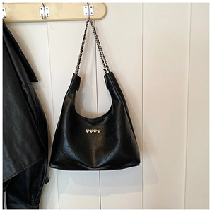 Detail of black faux leather hobo bag with heart studs and chain strap on a wooden hanger