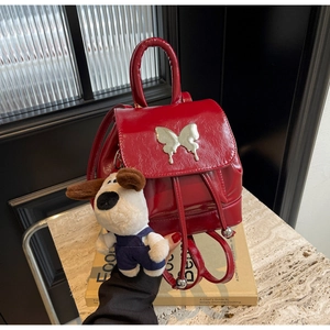 Détail d'un mini sac à dos en cuir verni rouge avec bijou papillon et pendentif de chien