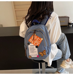 Detail of blue denim backpack featuring patchwork, embroidery and metal button accents