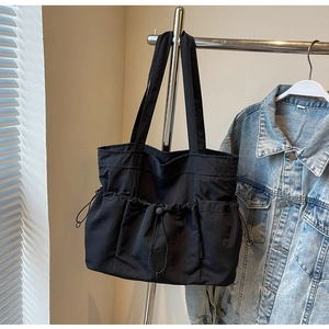 Detail of black pleated tote bag showing drawstring design and fabric texture on a hanger