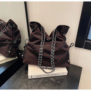 Close-up of black tote bag with red hearts, silver chain strap and side bow detail