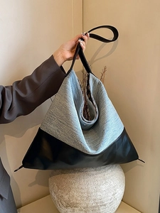 Large denim and black leather tote bag on stone pedestal against a beige background