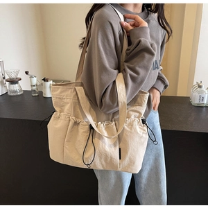 Detail of beige pleated canvas tote bag showing drawstring pockets and shoulder strap