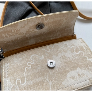 Detailed view of the magnetic metal buckle and vintage landscape print on beige crossbody bag