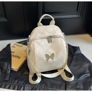 Detail of cream white quilted backpack featuring a silver butterfly logo on black backdrop
