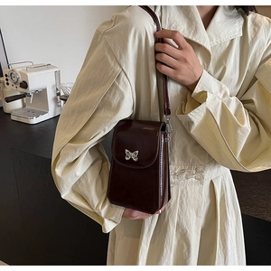 Detail of dark brown leather crossbody phone bag with silver butterfly buckle