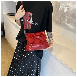 Detail of red patent leather shoulder bag with a bow accent and silver metal buckle