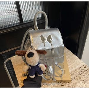 Détail d'un sac à dos argenté métallisé avec fermoir papillon et bijou de sac chien