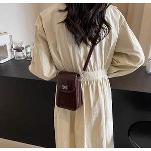 Detail of dark brown glossy crossbody phone bag with silver butterfly metal ornament