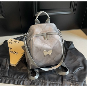 Detail of silver metallic quilted backpack featuring a decorative chrome butterfly
